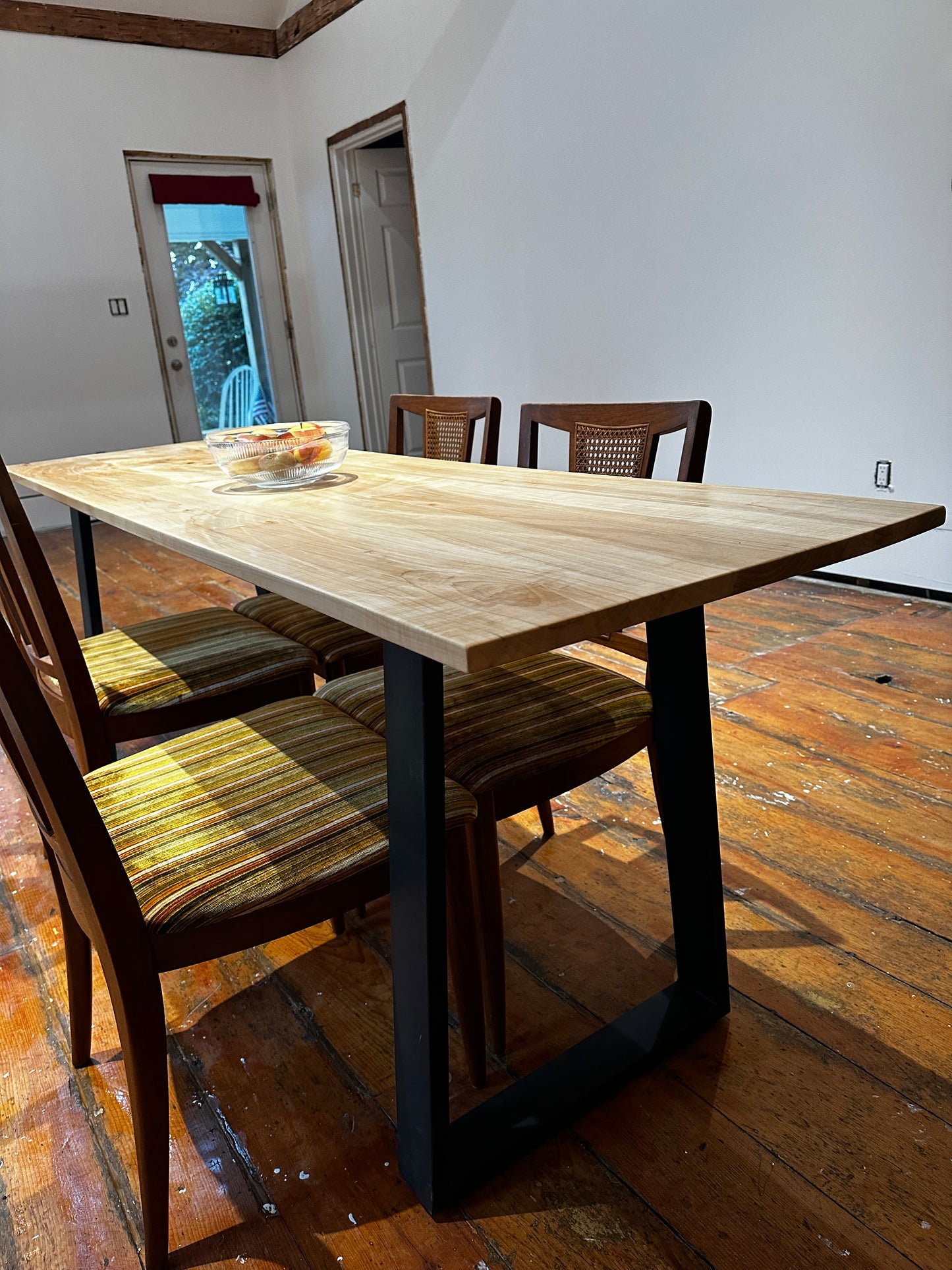 Wooden dining table with chairs in a room with wooden floor and white walls.