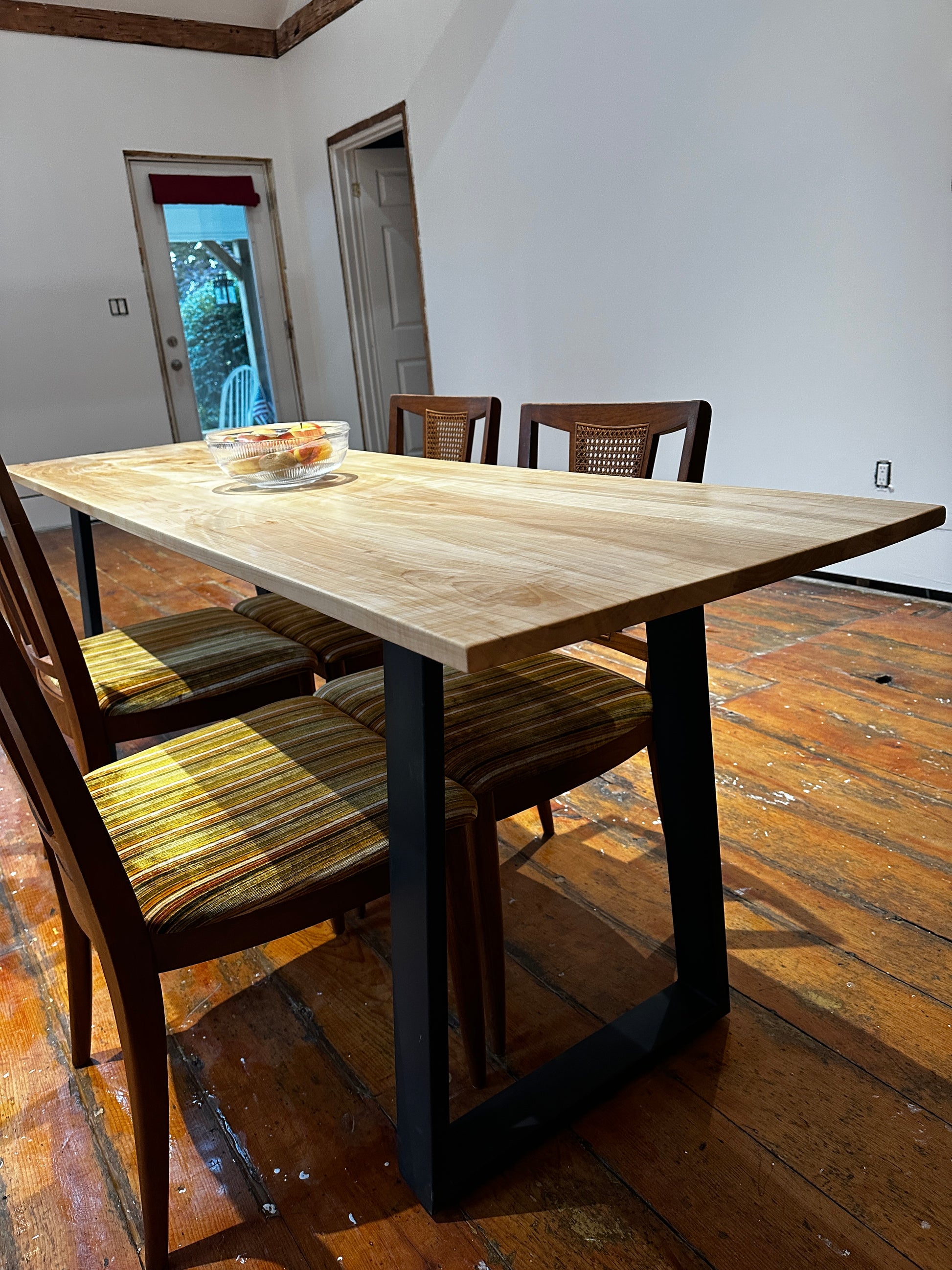 Wooden dining table with chairs in a room with wooden floor and white walls.