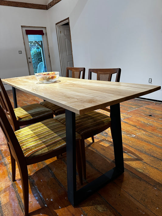 Wooden dining table with chairs in a room with wooden floor and white walls.